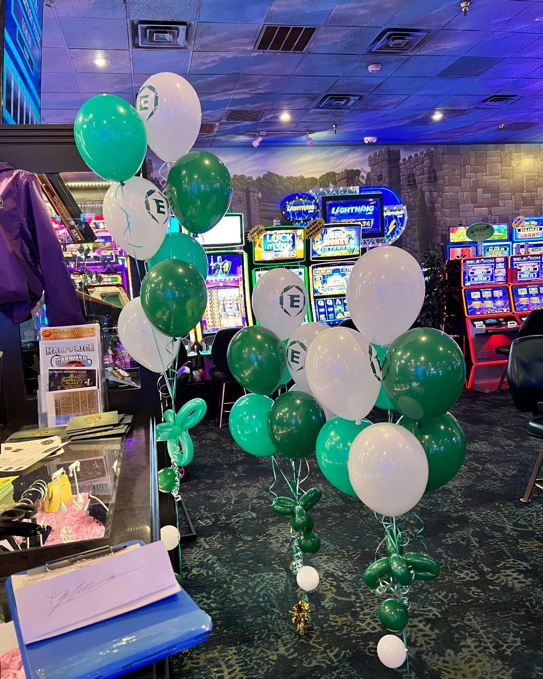 A bunch of green and white balloons are hanging from the ceiling in a casino.