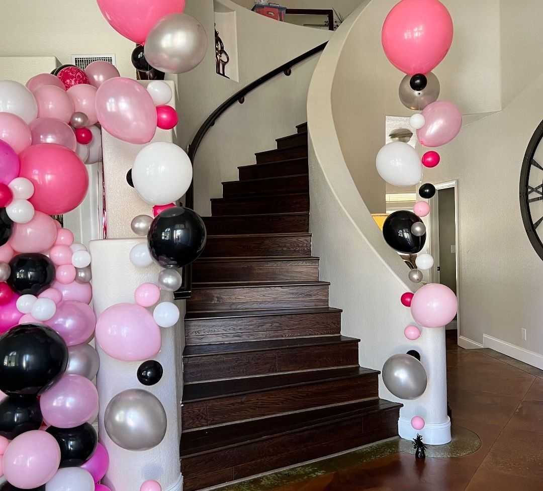 A spiral staircase is decorated with pink and black balloons