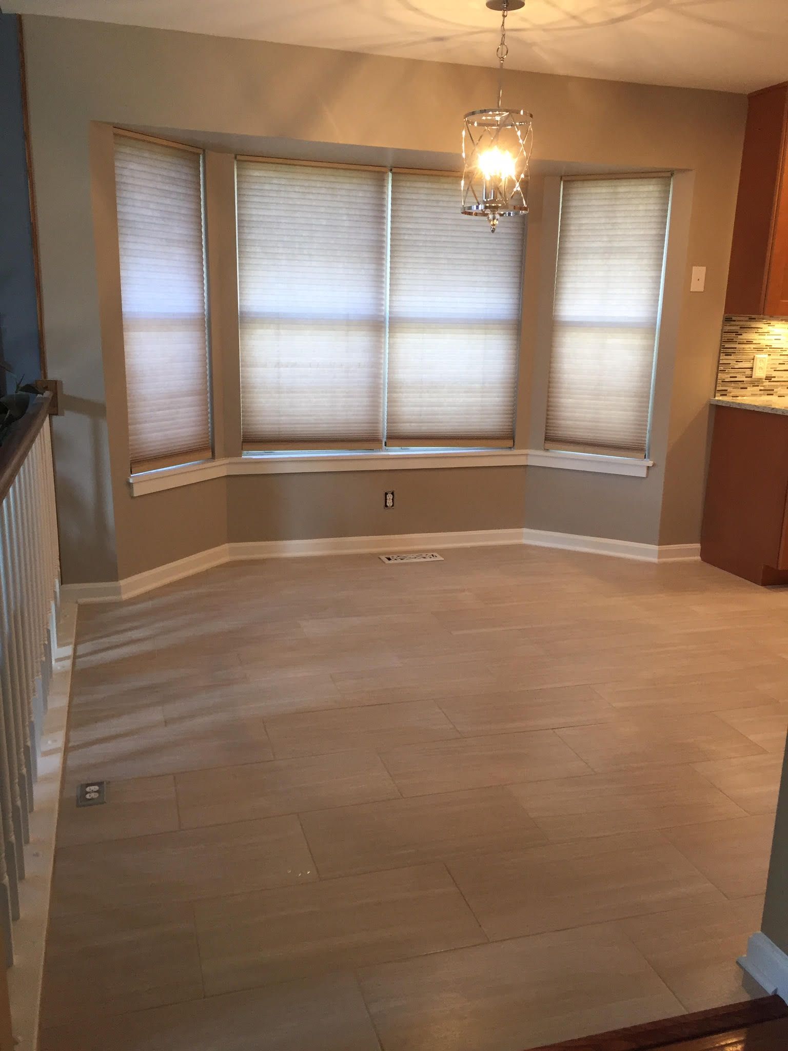 An empty dining room with a large bay window and a chandelier.