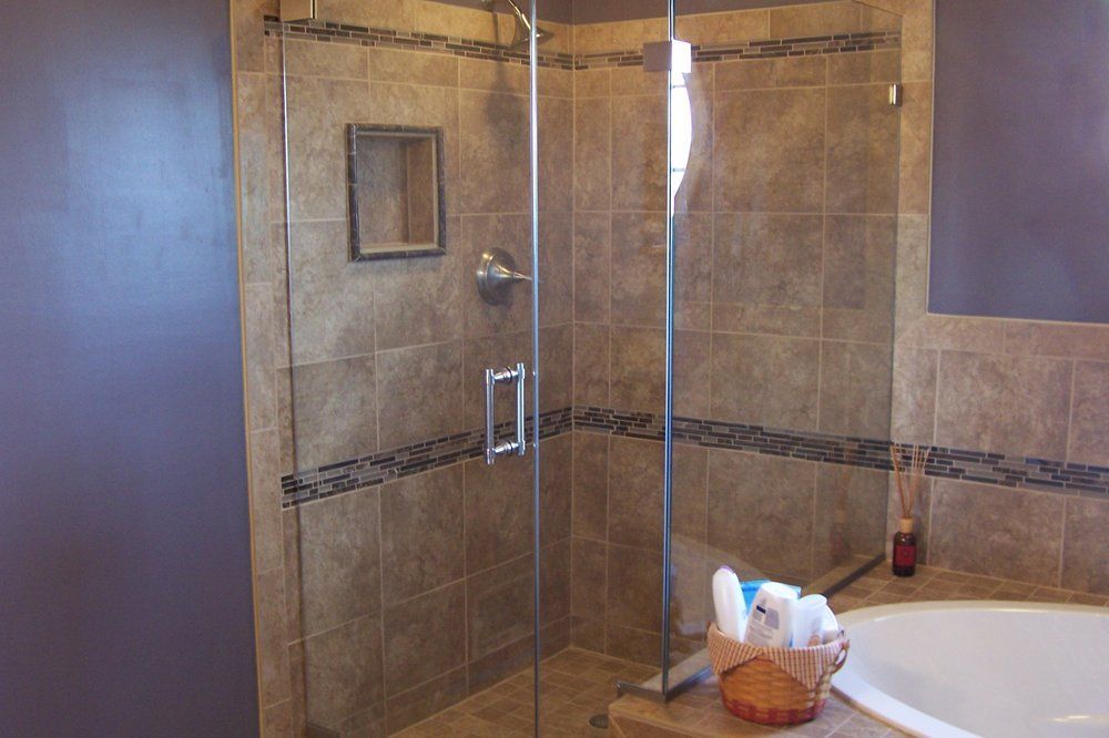 Glass shower enclosure with beige tile walls and a basket of toiletries in a bathroom.