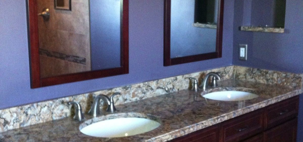 Bathroom with two sinks, granite countertop, brown cabinets, and purple walls.