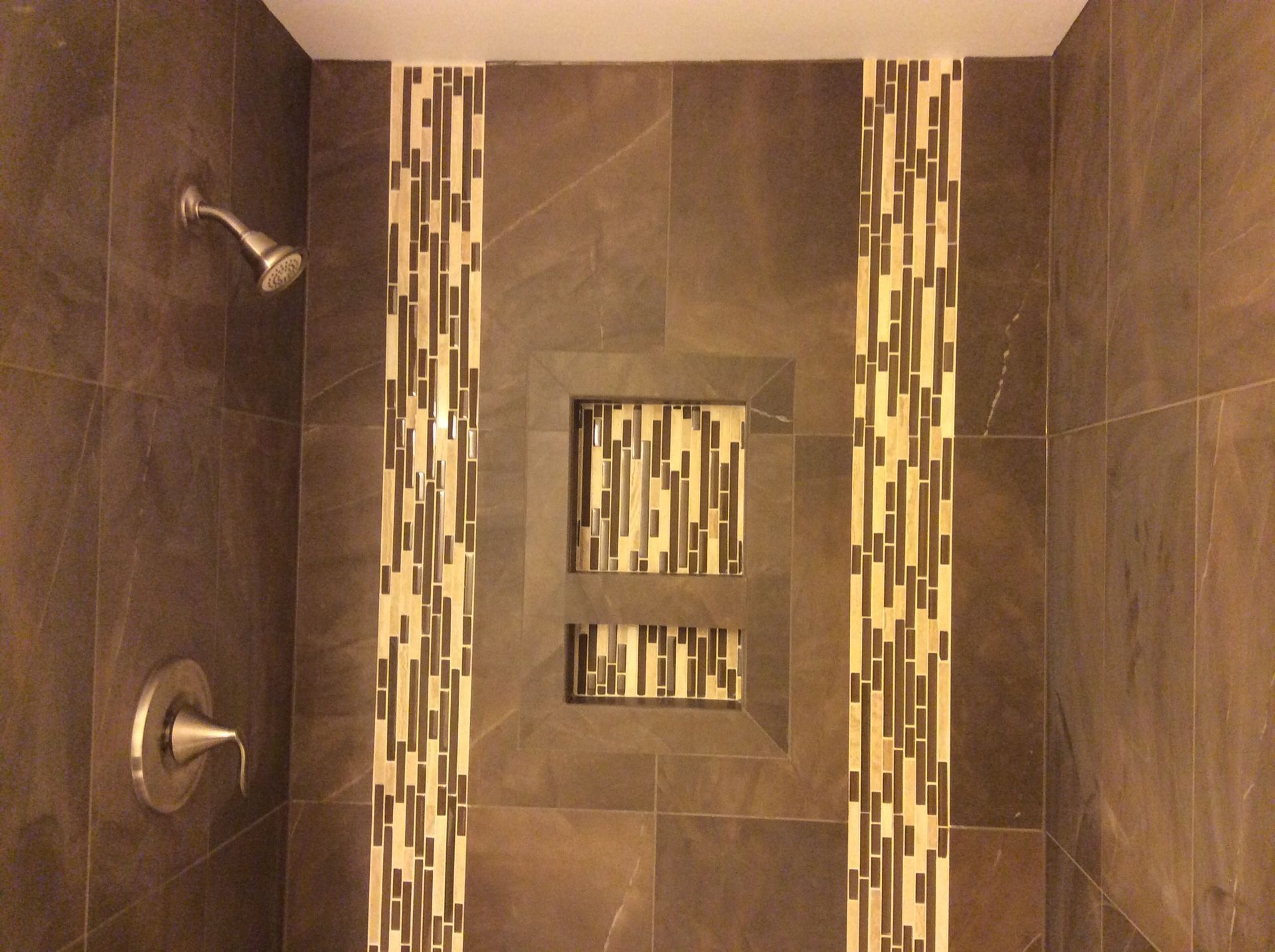 Dark brown tiled shower with decorative mosaic columns and recessed niches.
