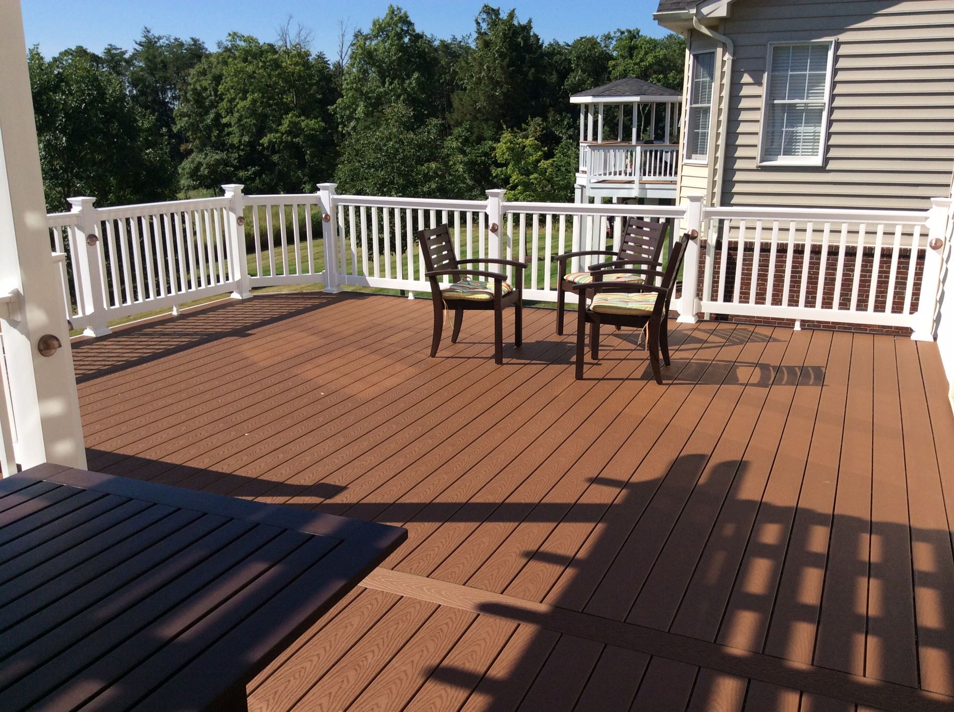 A wooden deck with a white railing and chairs
