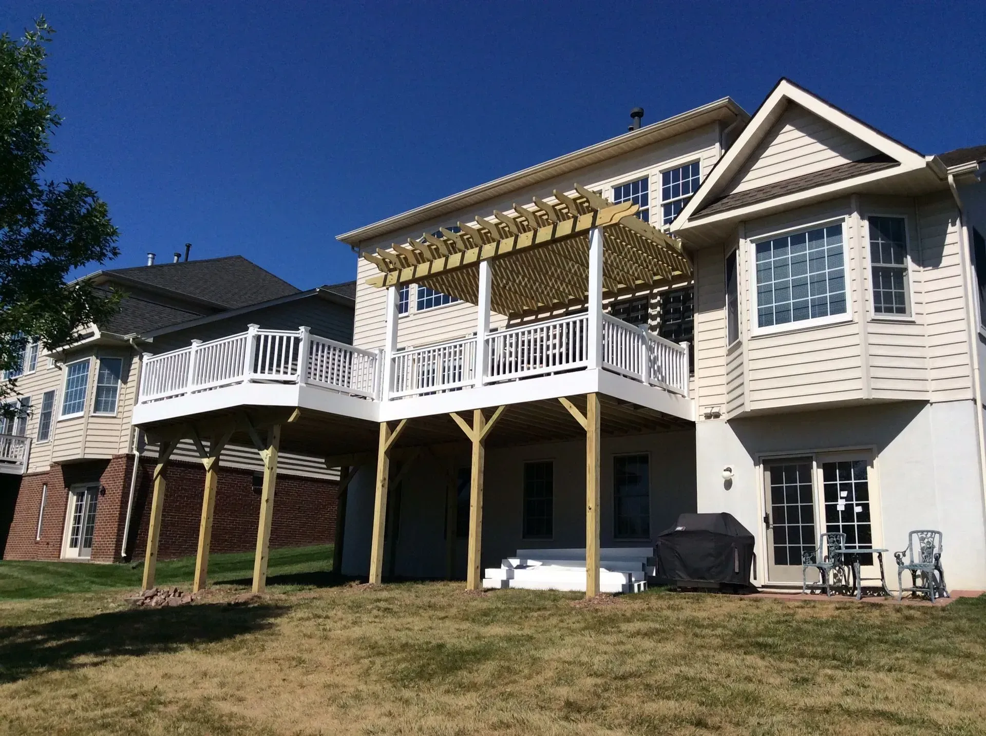 Multi-level deck on the back of a house with white railings, supported by wooden posts, against a blue sky.