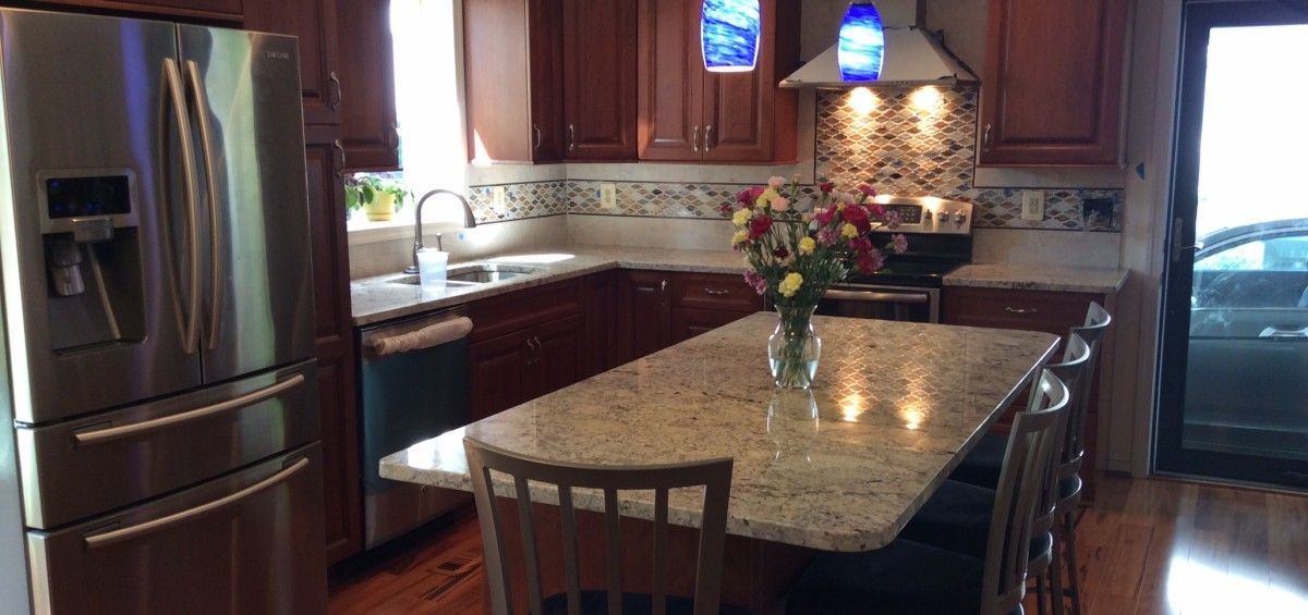 A kitchen with a stainless steel refrigerator, island with chairs, and flowers on the counter.