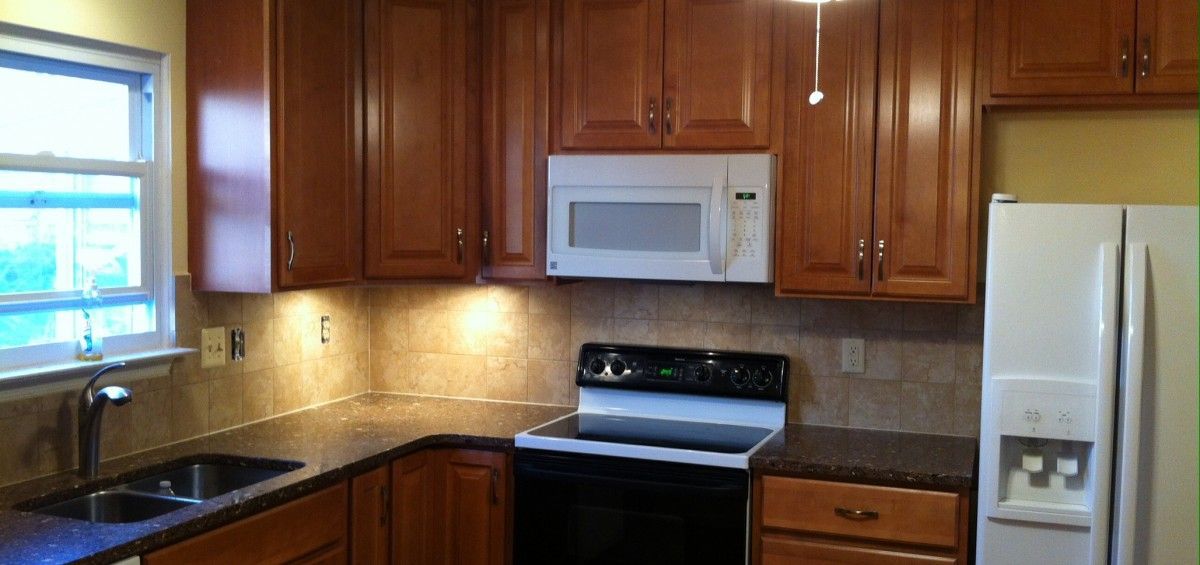 Kitchen with wooden cabinets, a microwave, and a white refrigerator. The countertop is dark.