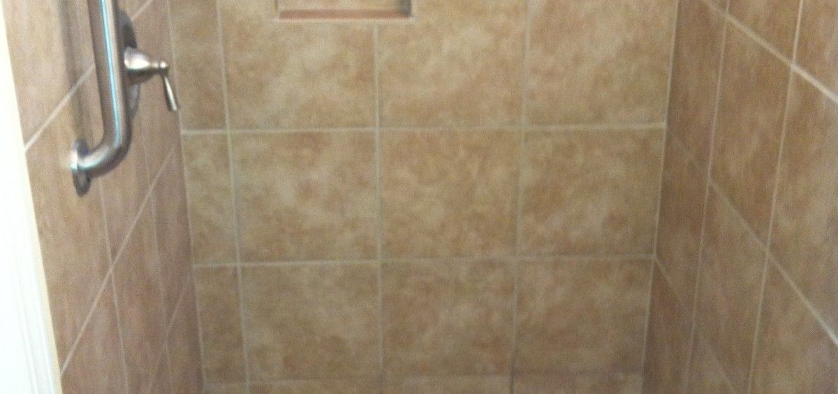 Brown tiled shower with a niche and shower fixture.