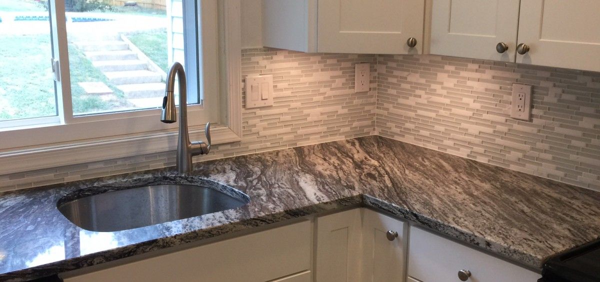 Kitchen with white cabinets, stone countertop, tile backsplash, and stainless steel sink with a window view.