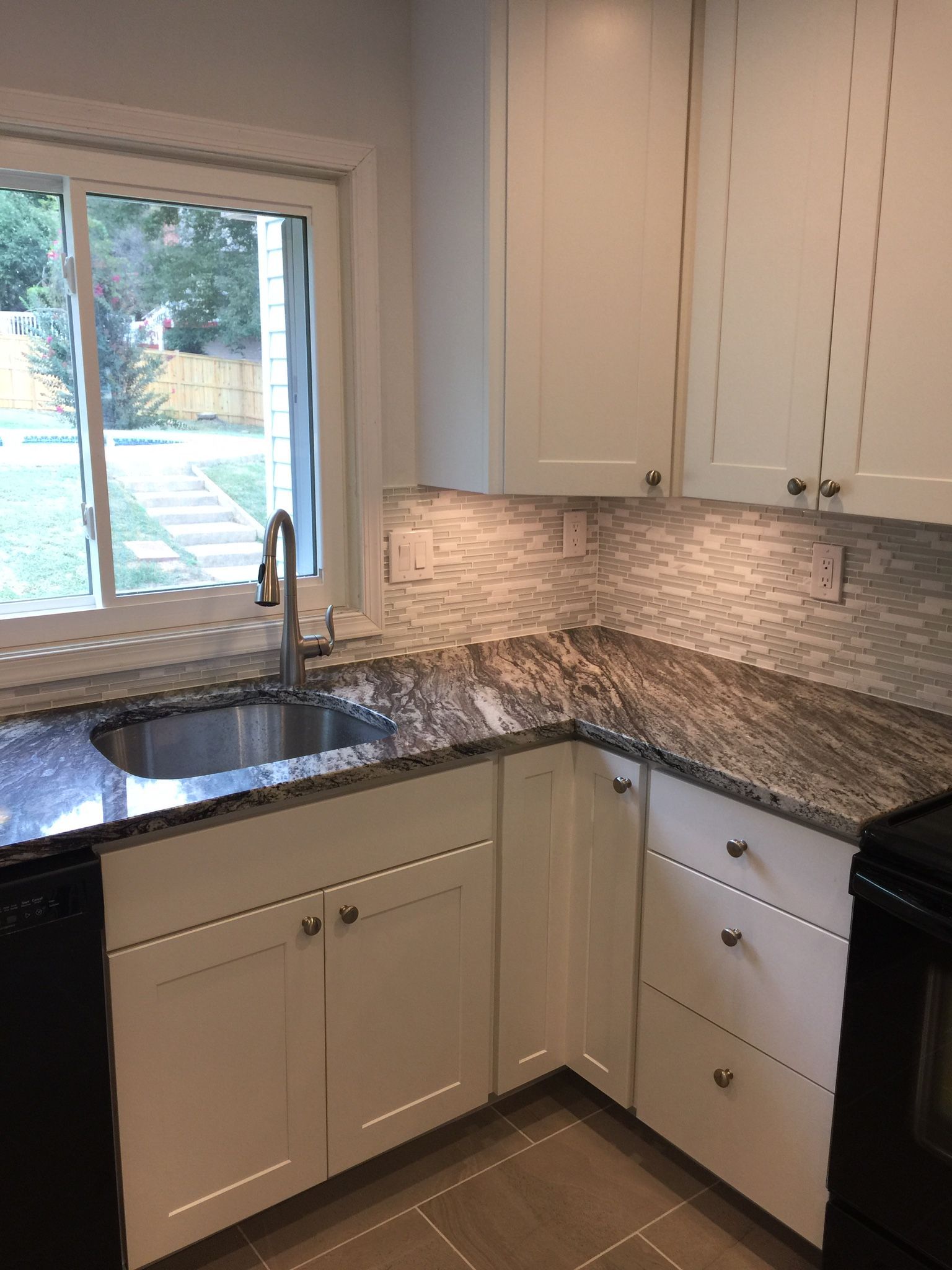 White kitchen cabinets with granite countertop, sink under a window.