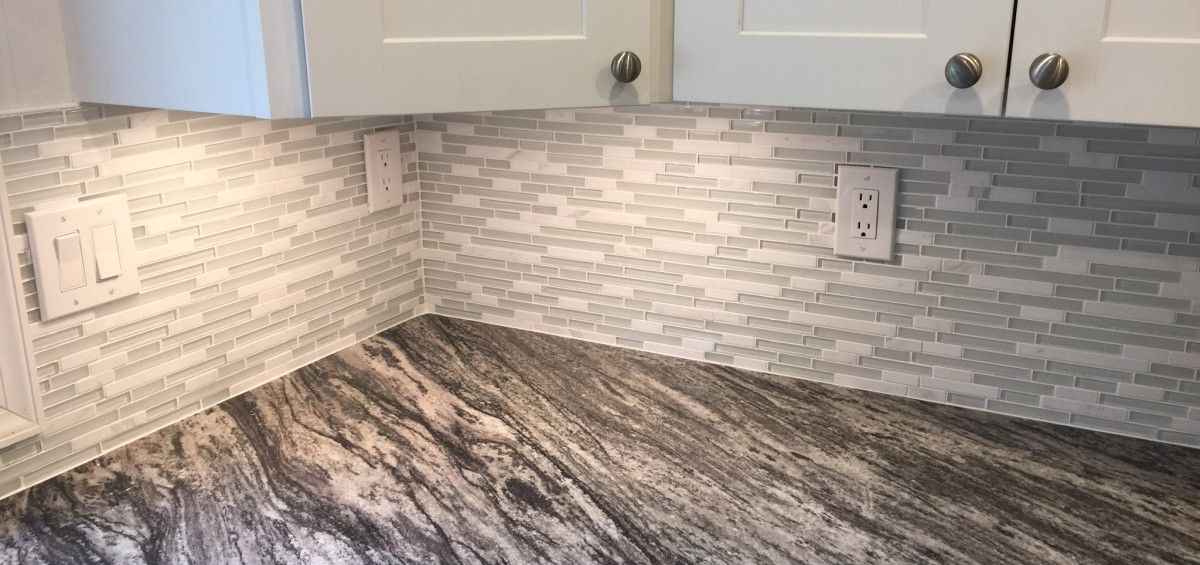 A kitchen corner featuring a tiled backsplash, granite countertop, white cabinets, and outlets.