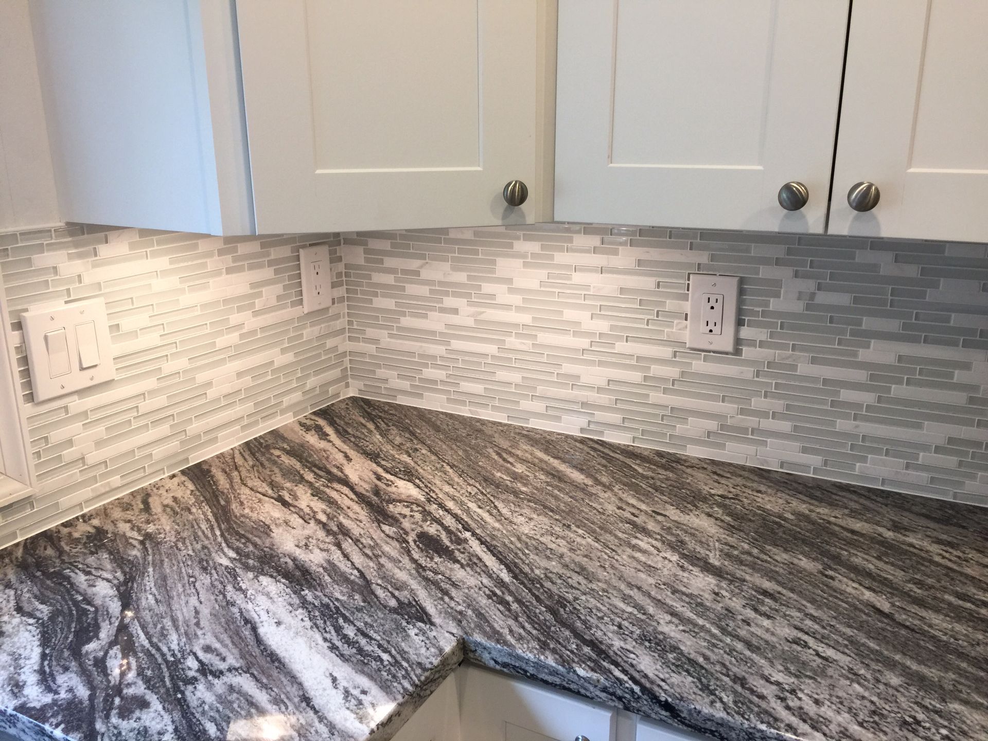 Kitchen countertop with granite, mosaic backsplash, white cabinets, and outlets.