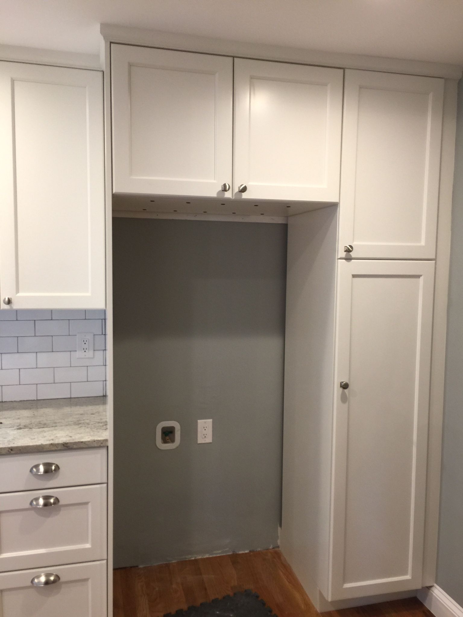 White kitchen cabinets surround a grey refrigerator space with electrical outlets.