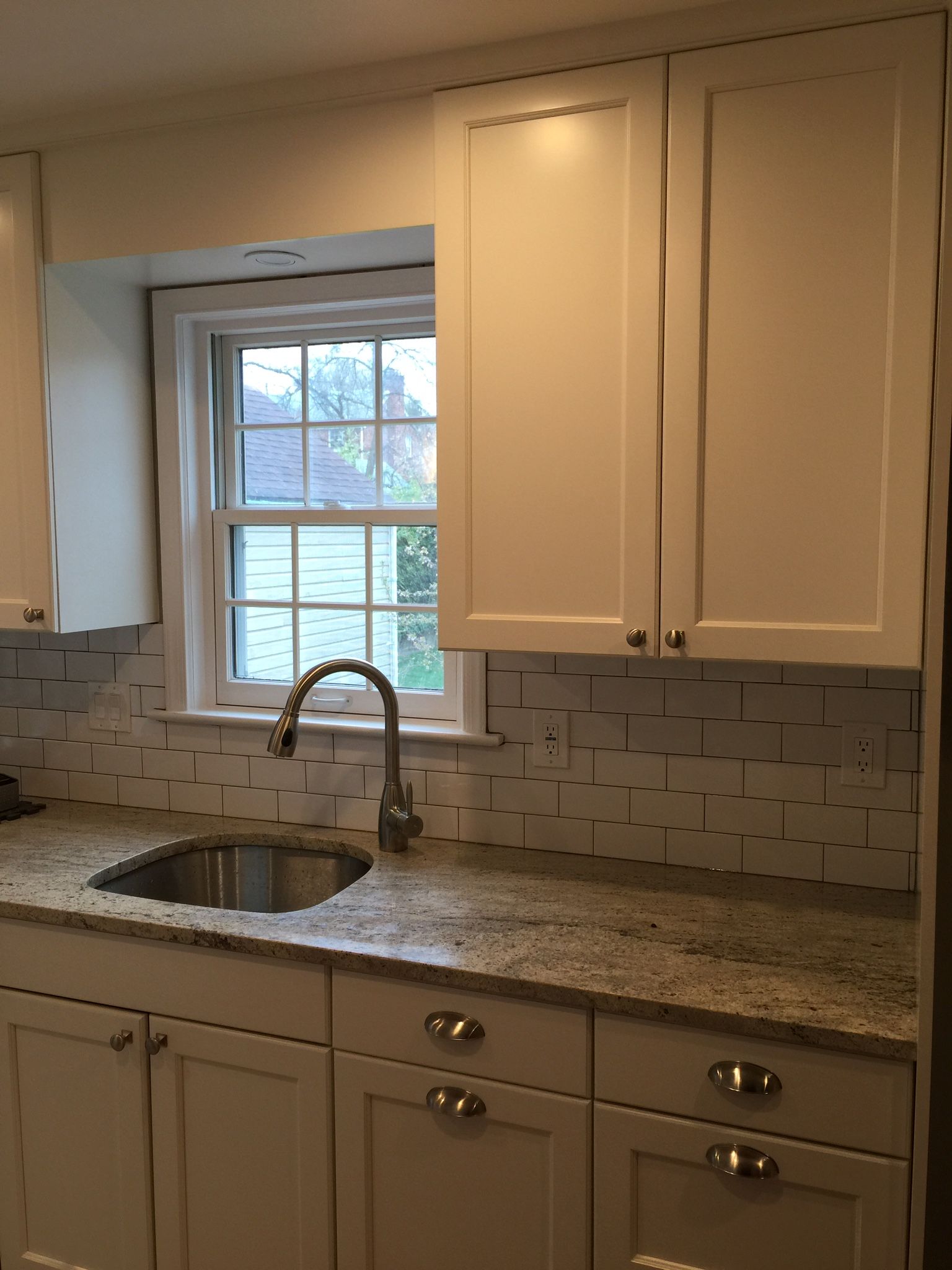 Kitchen with white cabinets, granite countertop, stainless steel sink, and a window.