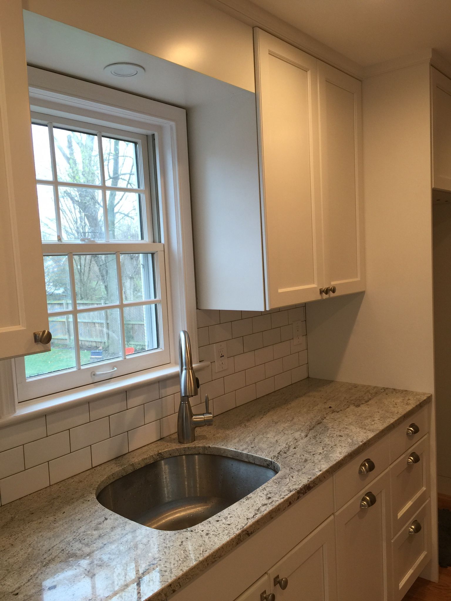 Kitchen sink area with a window, white cabinets, and granite countertop.