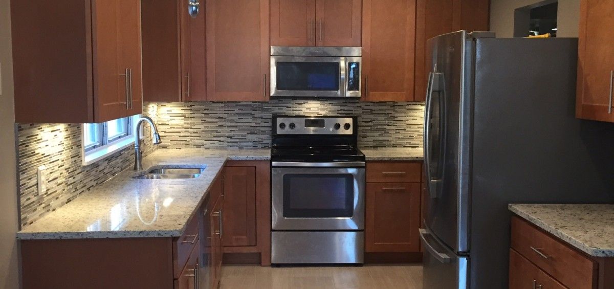 A kitchen with brown cabinets, stainless steel appliances, granite countertops, and a tiled backsplash.