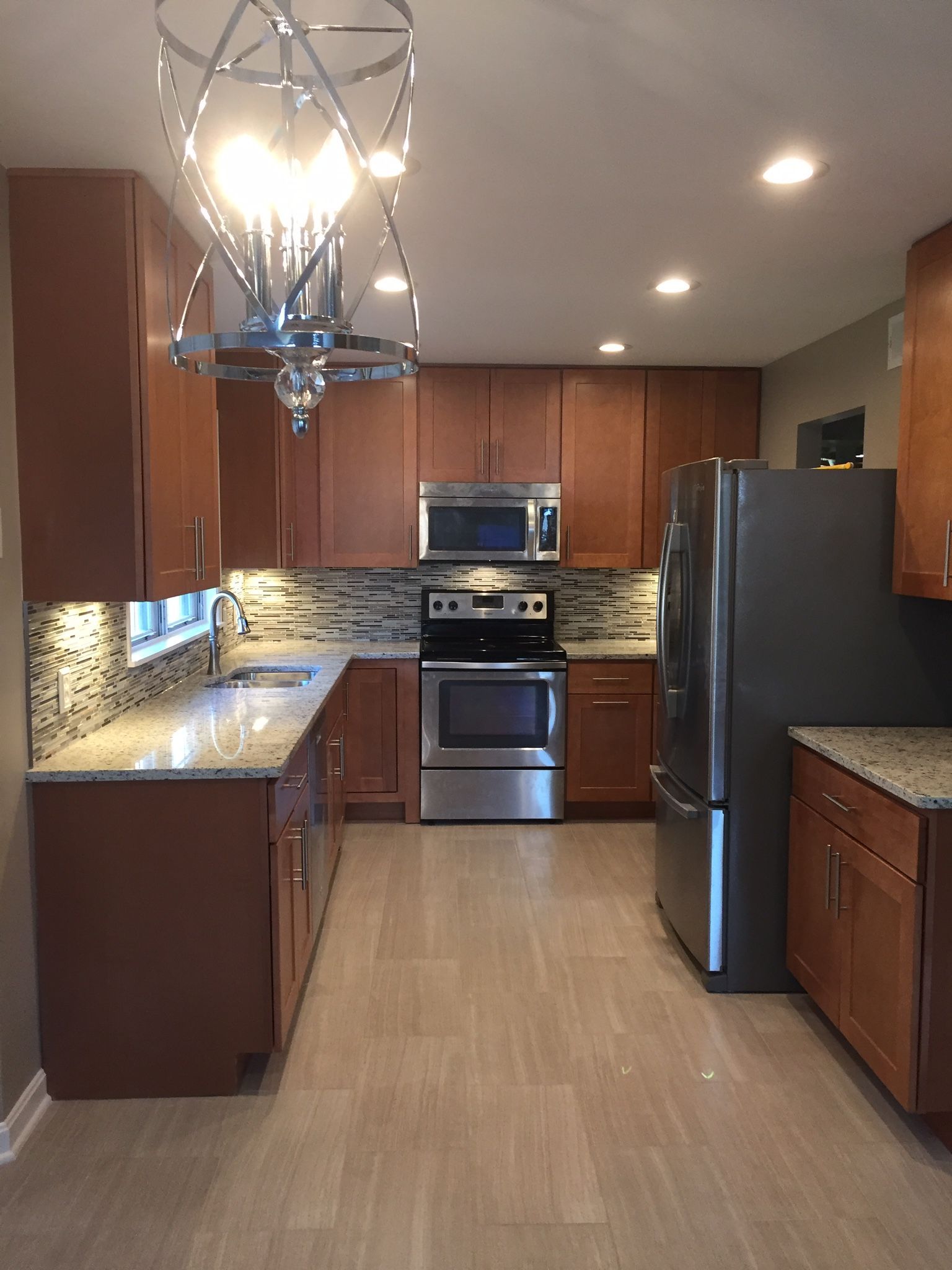 A modern kitchen with brown cabinets, stainless steel appliances, granite countertops, and tiled backsplash.