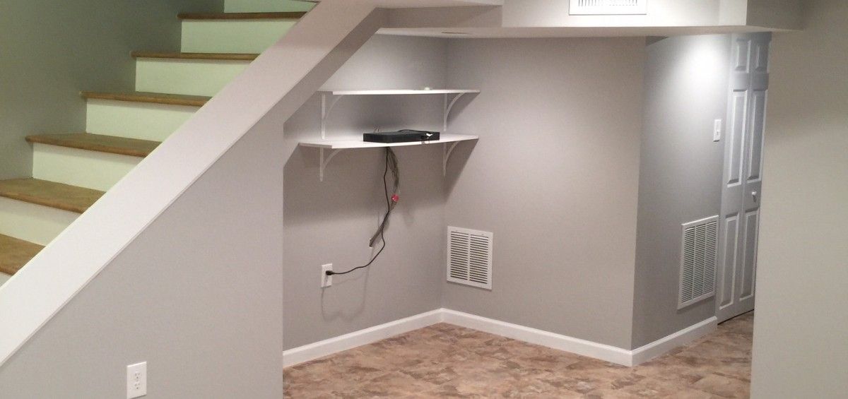 A basement with stairs and a shelf under the stairs.