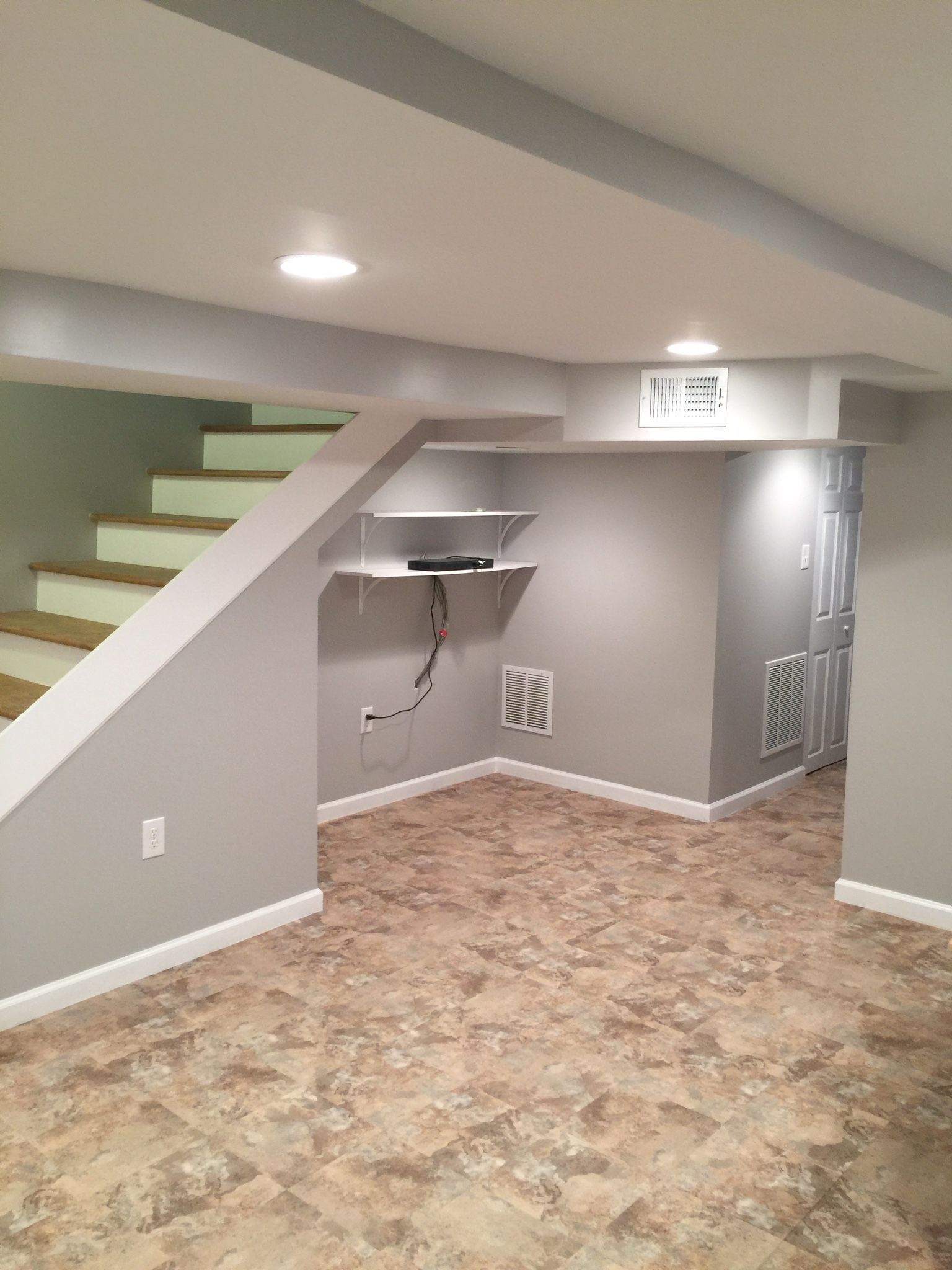 Finished basement with stairs, shelves, and beige flooring. Gray walls and white ceiling.