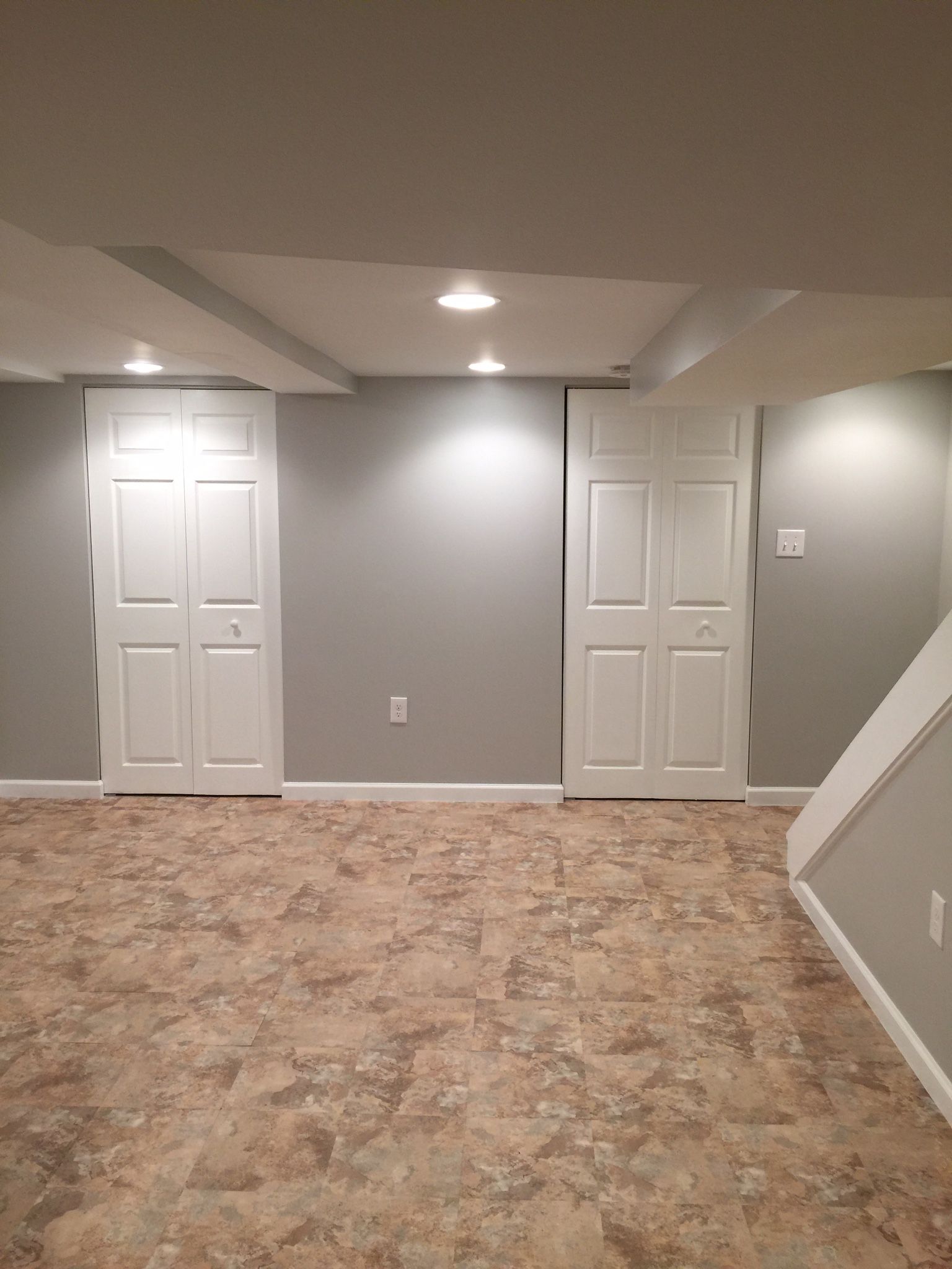 A finished basement with two white closet doors, gray walls, brown flooring, and recessed lighting.