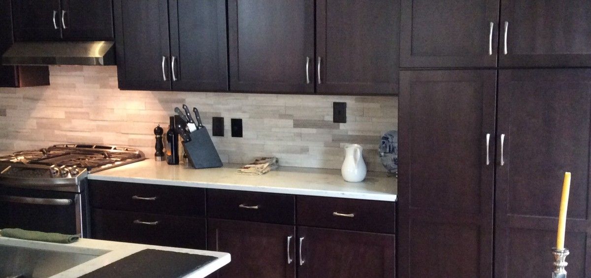 Dark wooden kitchen cabinets with a light backsplash, stove, and countertop.