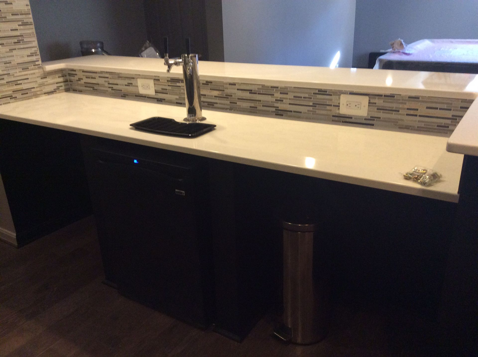 Bar with white countertop, dark cabinets, a tap, and a stainless steel trash can.