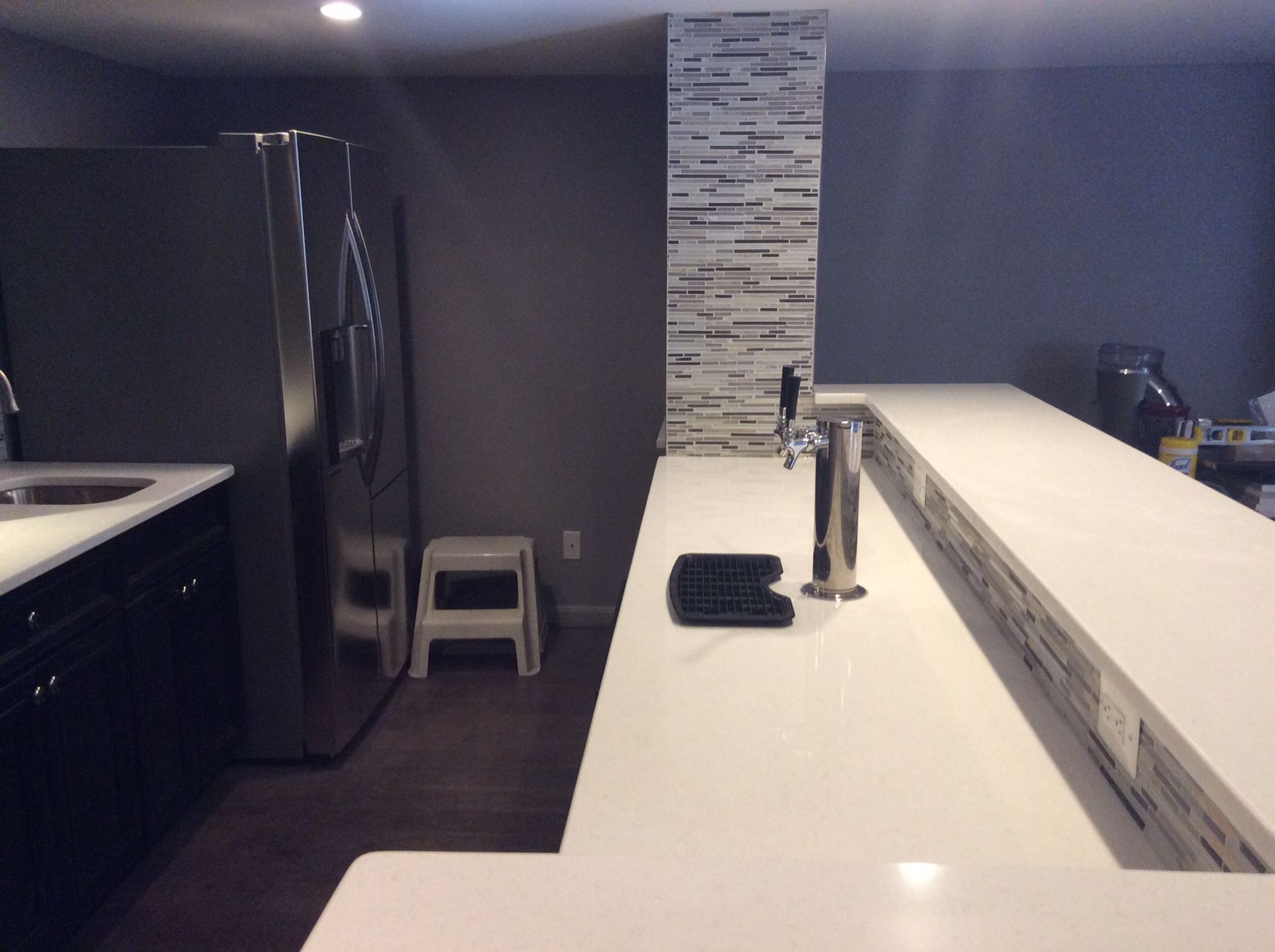 Kitchen with a white countertop bar, fridge, and a dark cabinet.
