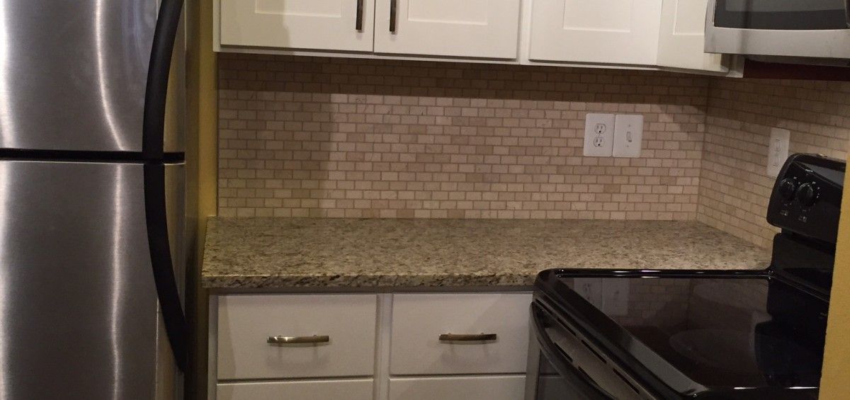 Kitchen view with white cabinets, stainless steel refrigerator, and tiled backsplash.