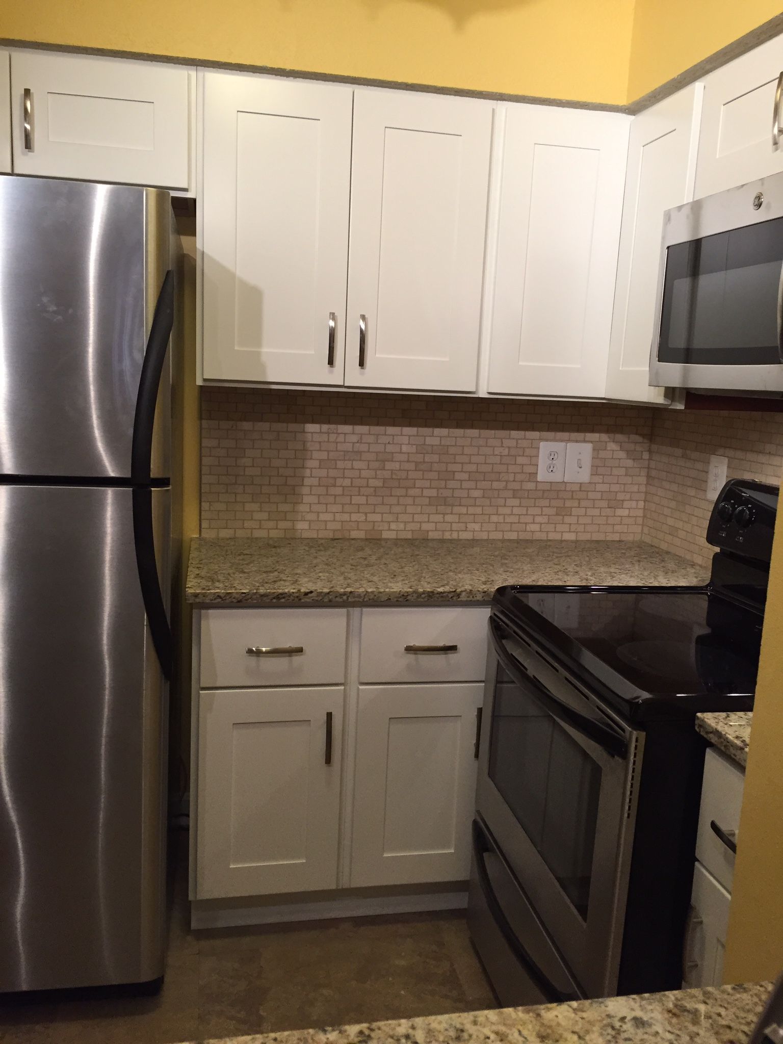 A kitchen with white cabinets, stainless steel appliances, and a granite countertop against a yellow wall.