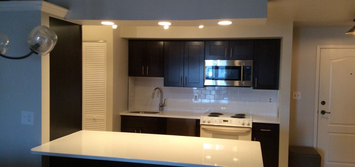 A kitchen featuring dark cabinets, white countertops, and stainless steel appliances.