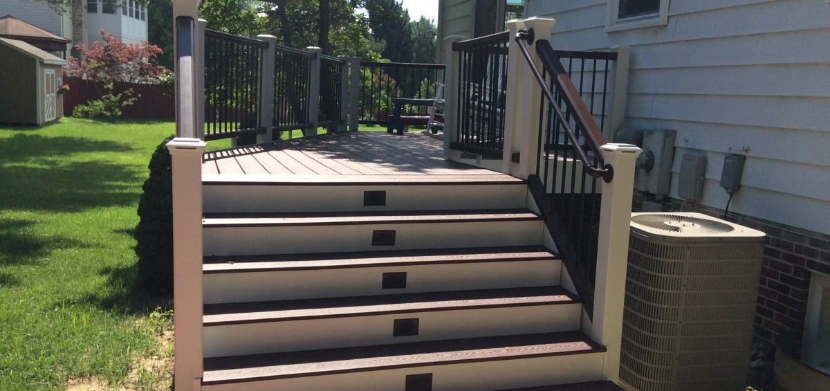 Wooden deck stairs leading to a deck with an attached house on the right and a yard on the left.