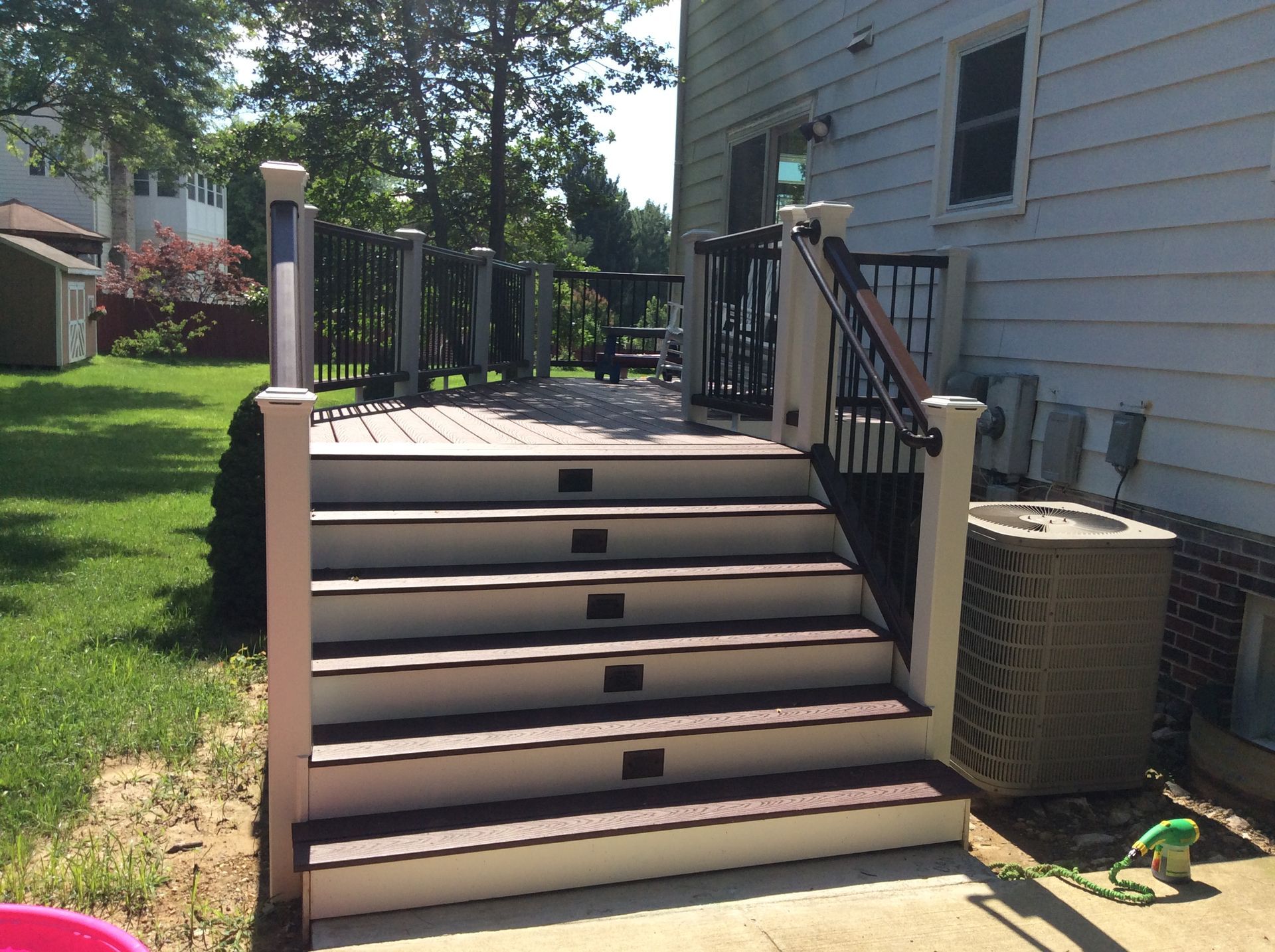 Deck with stairs leading up to it, next to a house, green grass.
