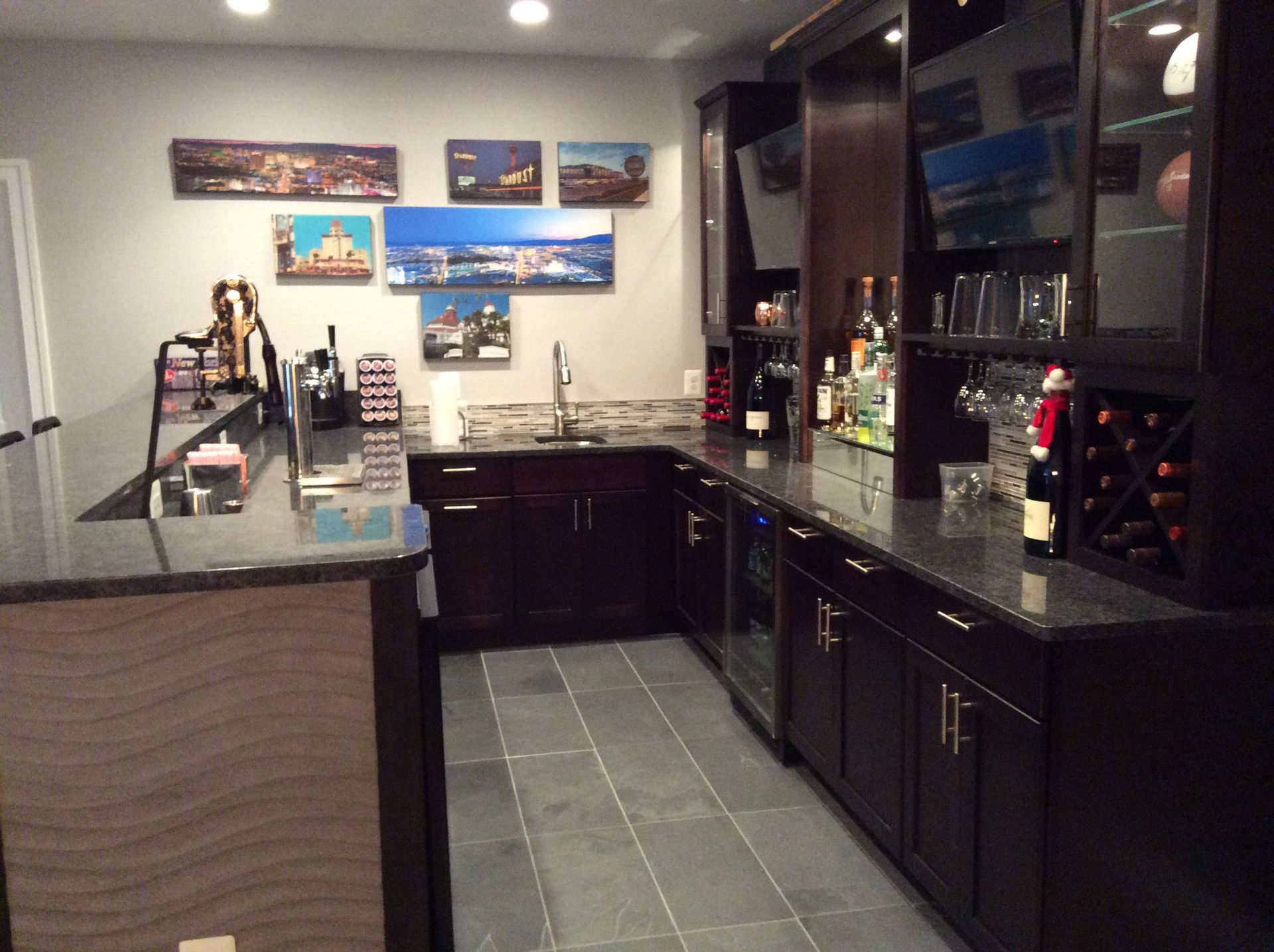 Dark-wood home bar with granite countertops, a sink, and drink storage, with art on the wall.