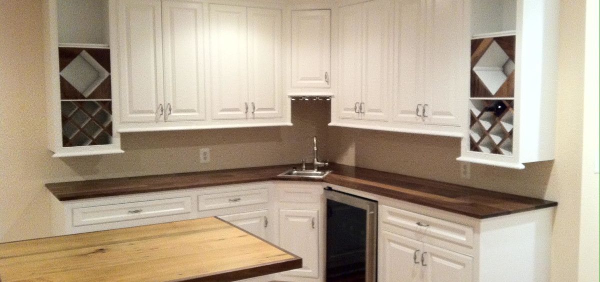 White cabinets with dark wood countertop in a kitchen. Wine rack, sink, and wine cooler.
