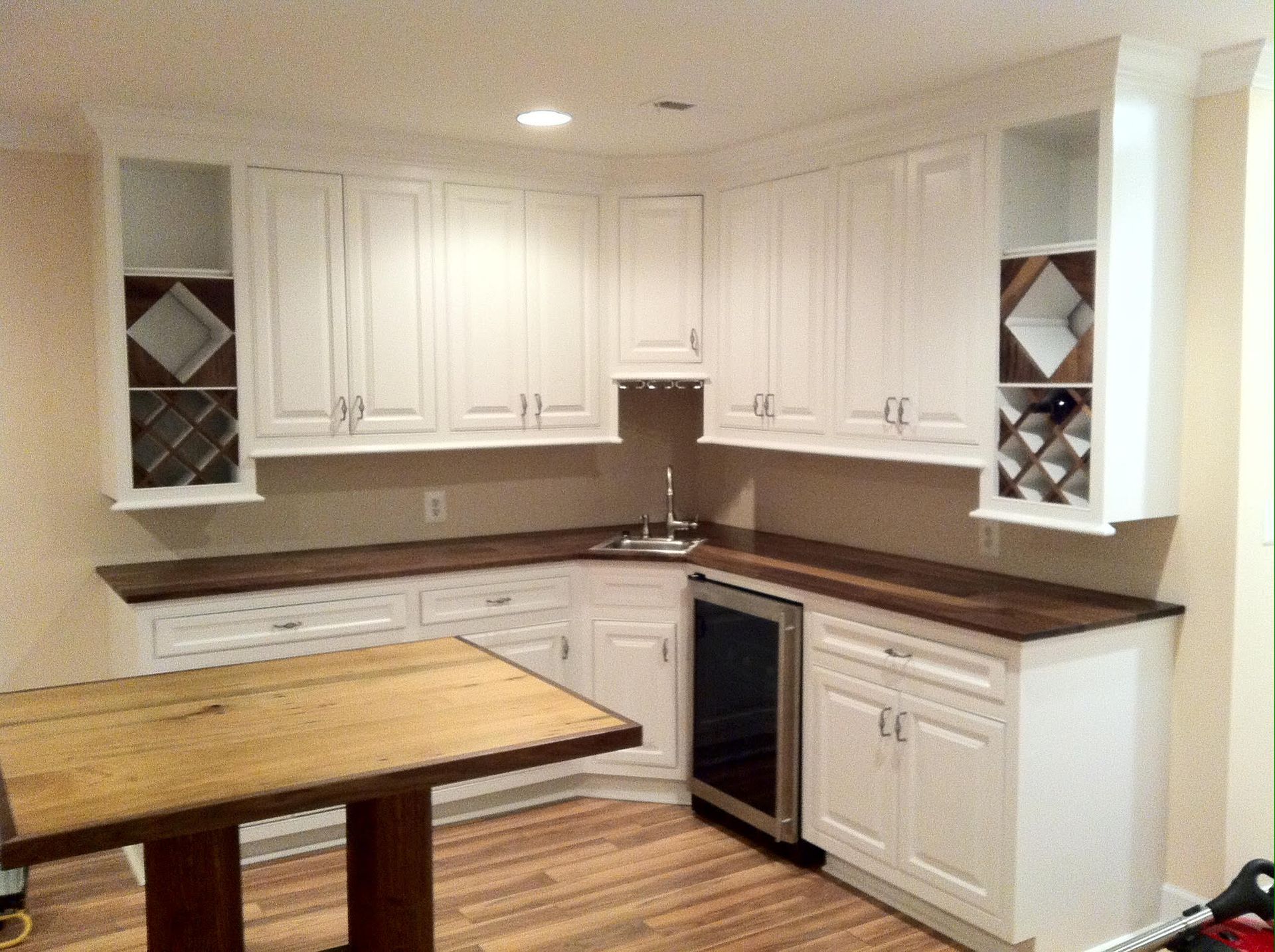 White cabinets in a home bar with wood countertops, a wine fridge, and a small table.