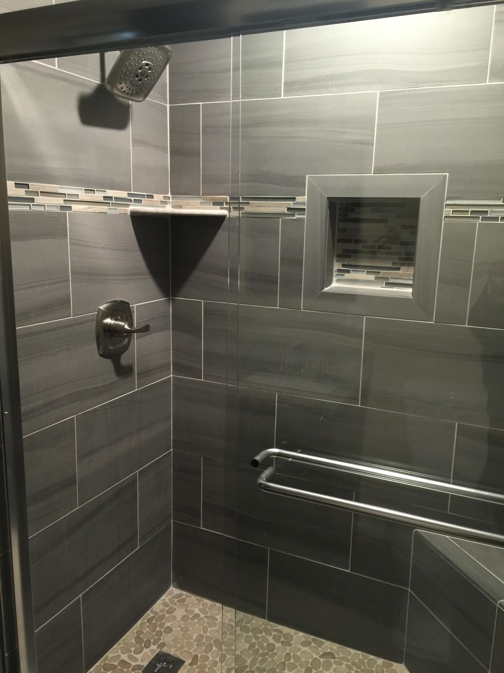 Gray tiled shower with a shelf, niche, and grab bar.