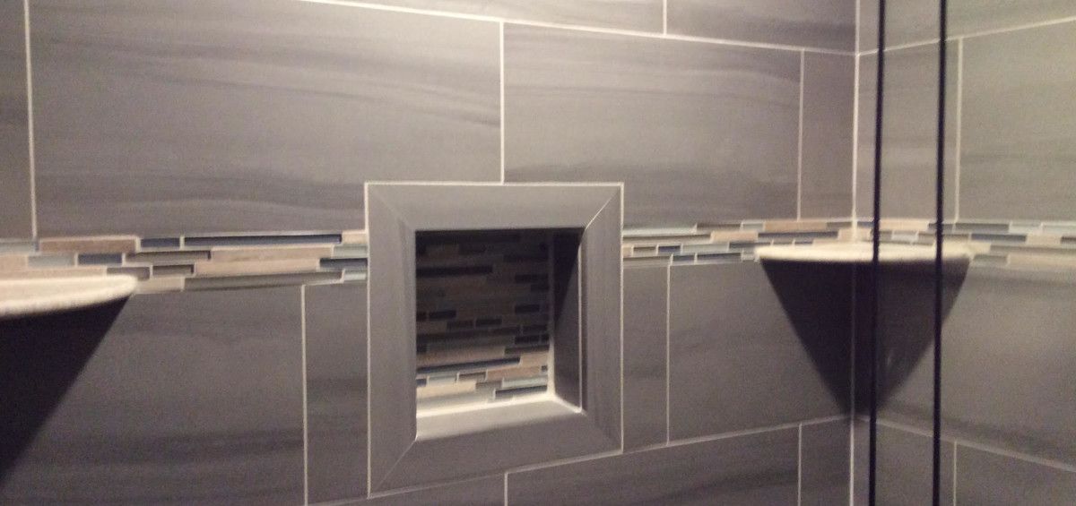 Shower wall with a recessed shelf and two corner shelves, all tiled in gray stone.