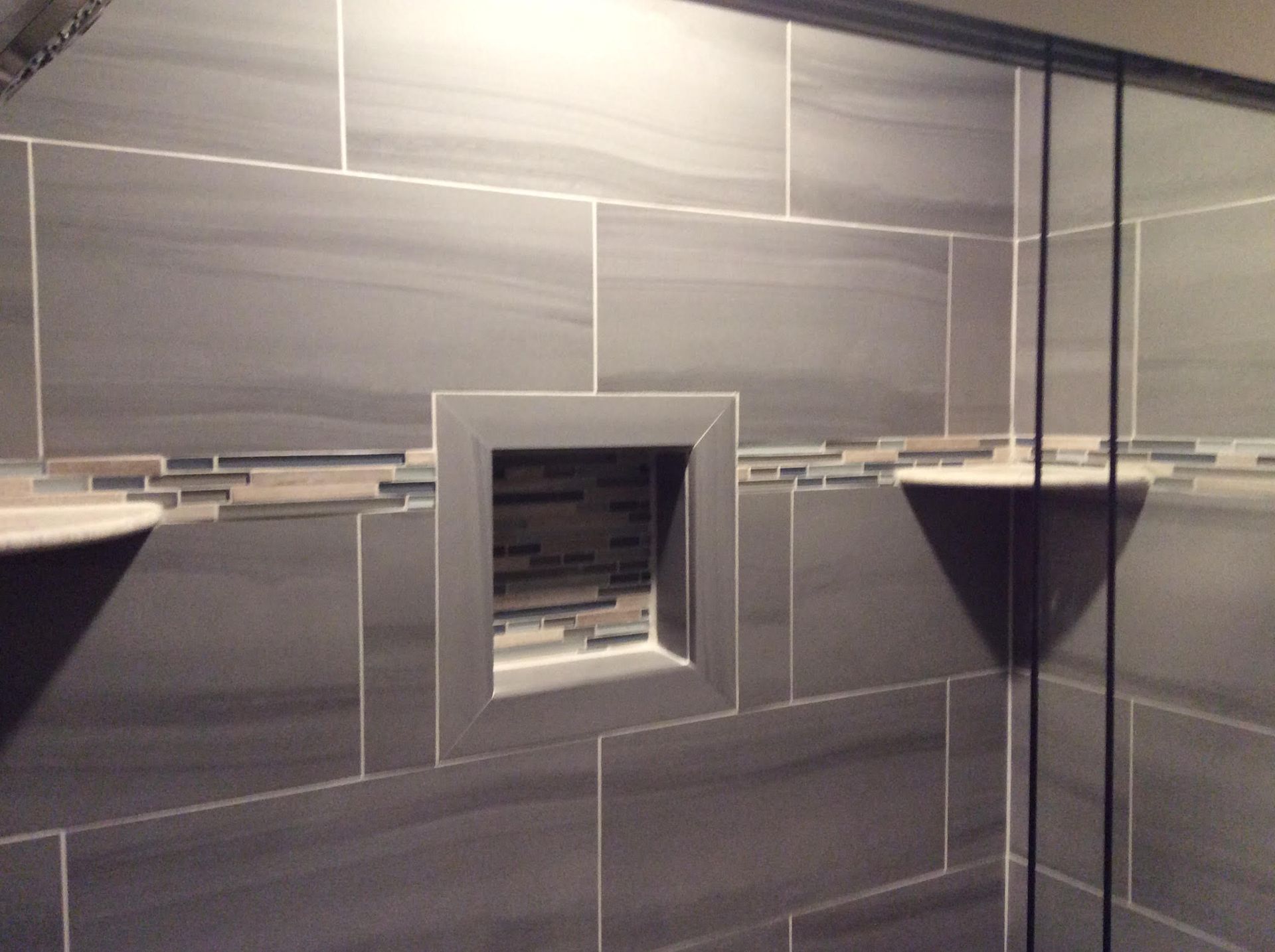 Dark gray tiled shower with built-in niche and shelves; glass shower door on the right.