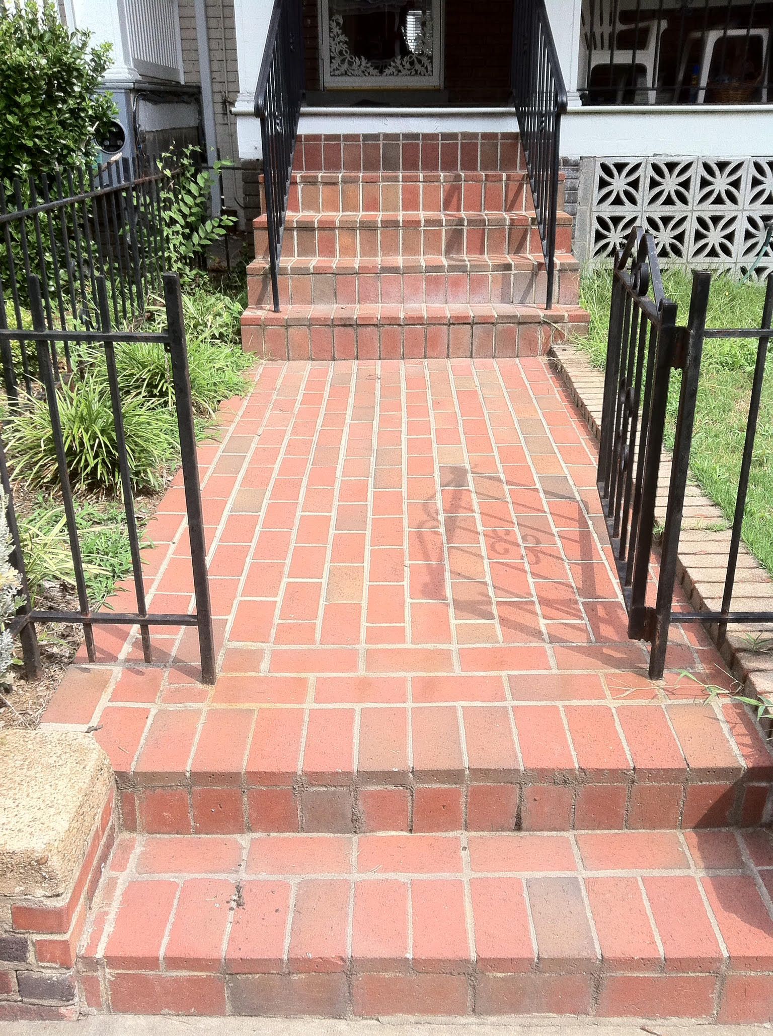 Brick steps and walkway leading to a house with black railings and a hay bale on the side.