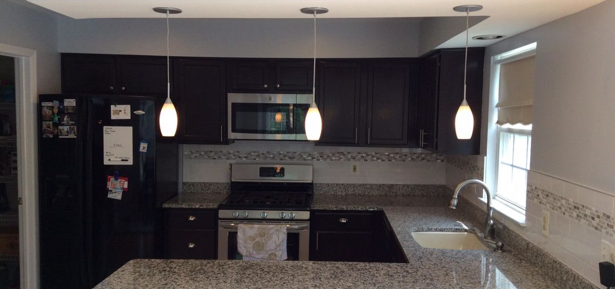 Kitchen with dark cabinetry, stainless steel appliances, granite countertops, and pendant lighting.