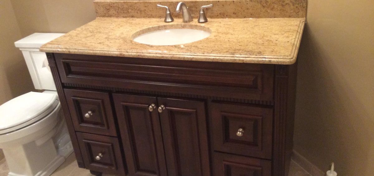 Bathroom vanity with a dark wood cabinet, tan countertop, and white sink. A toilet is next to the vanity.