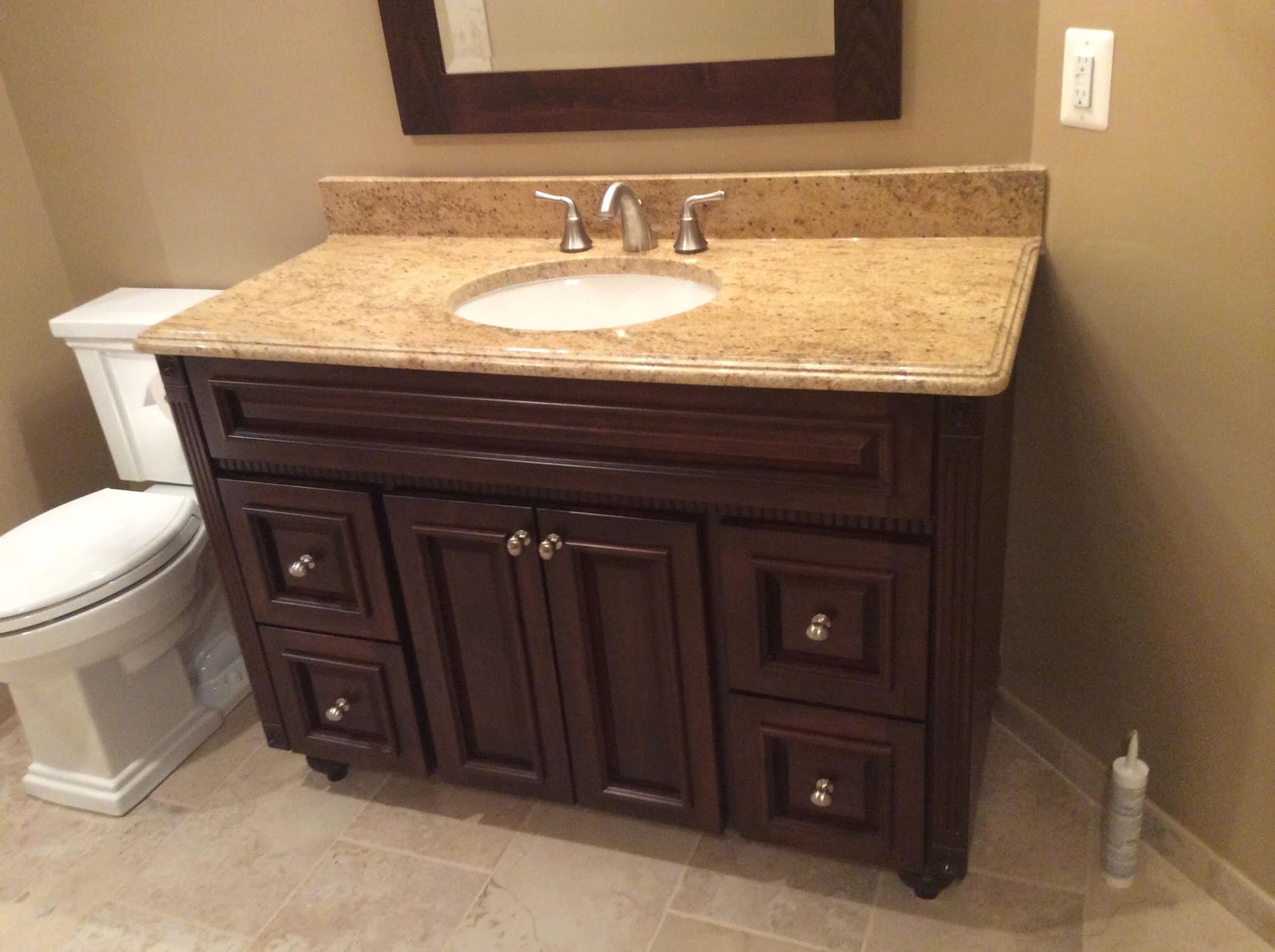 Dark wood bathroom vanity with tan countertop, white sink, and toilet.