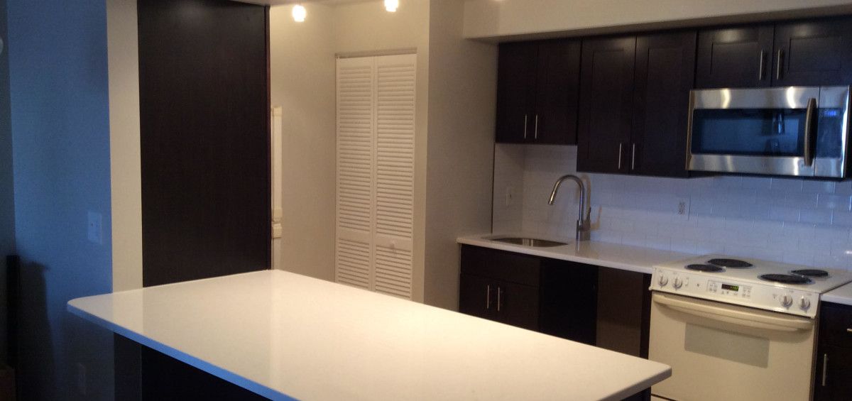 Modern kitchen with dark cabinets, white countertops, and a large island.