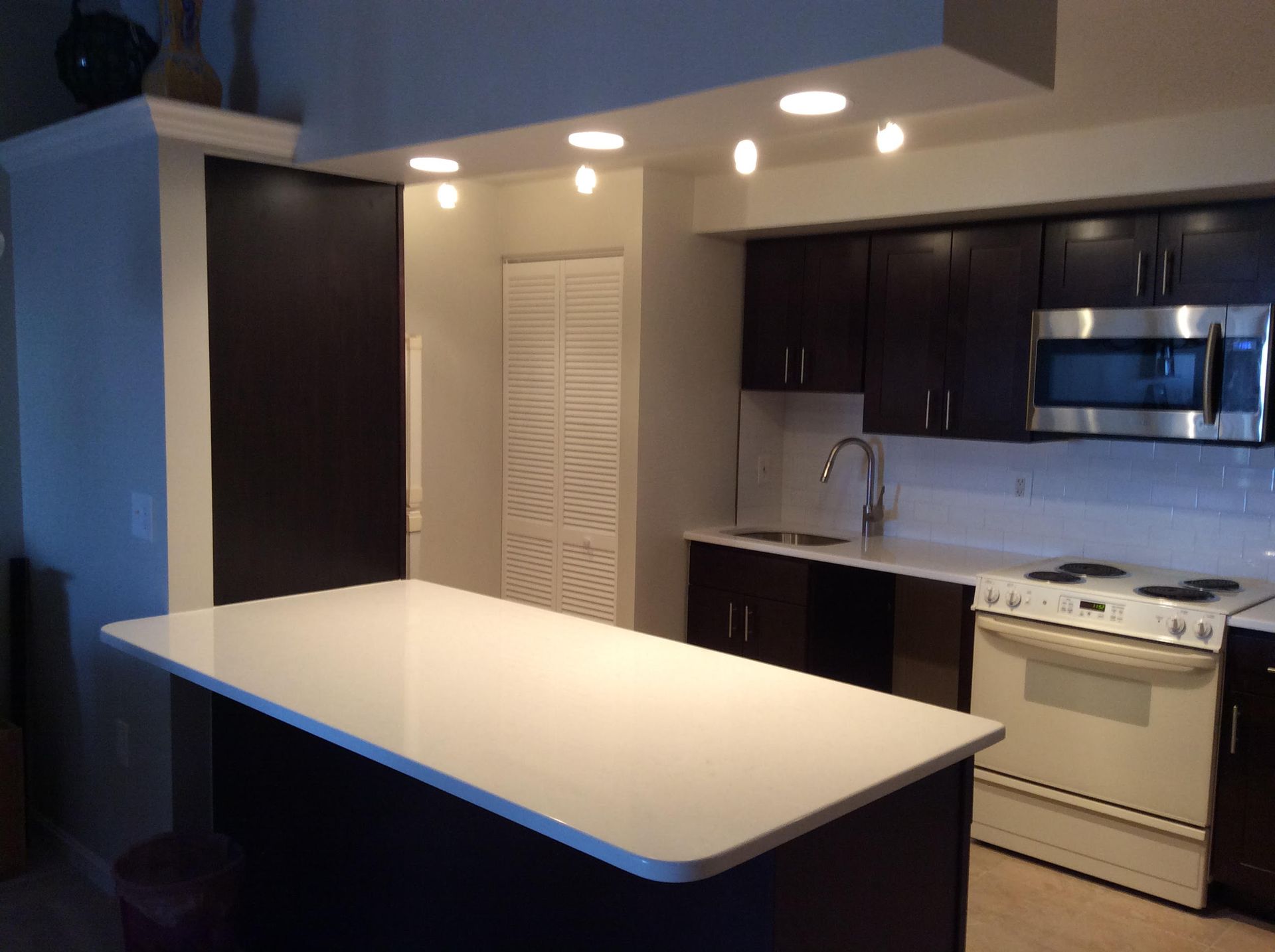 Modern kitchen with white countertop island, dark cabinets, and stainless steel appliances.