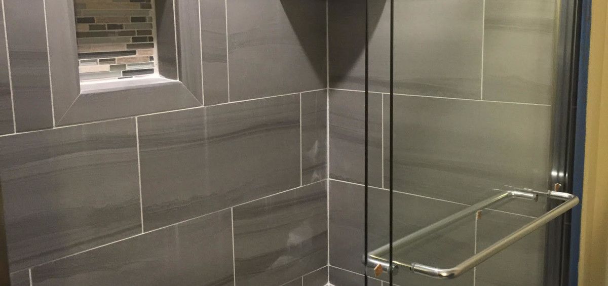 A tiled shower with a glass door, a shelf, and a silver handle.