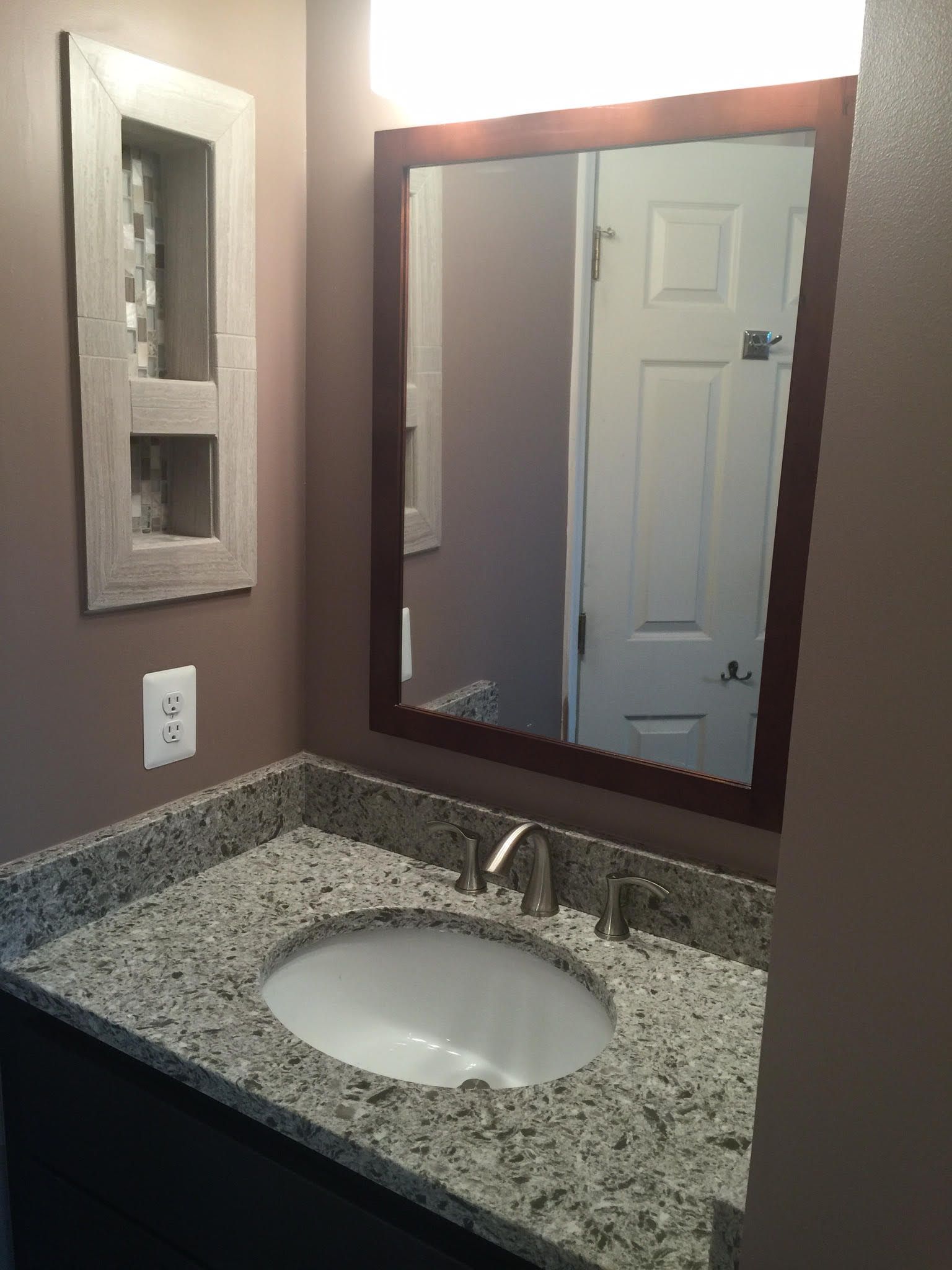 Bathroom with brown walls, granite countertop, white sink, and dark wood-framed mirror.