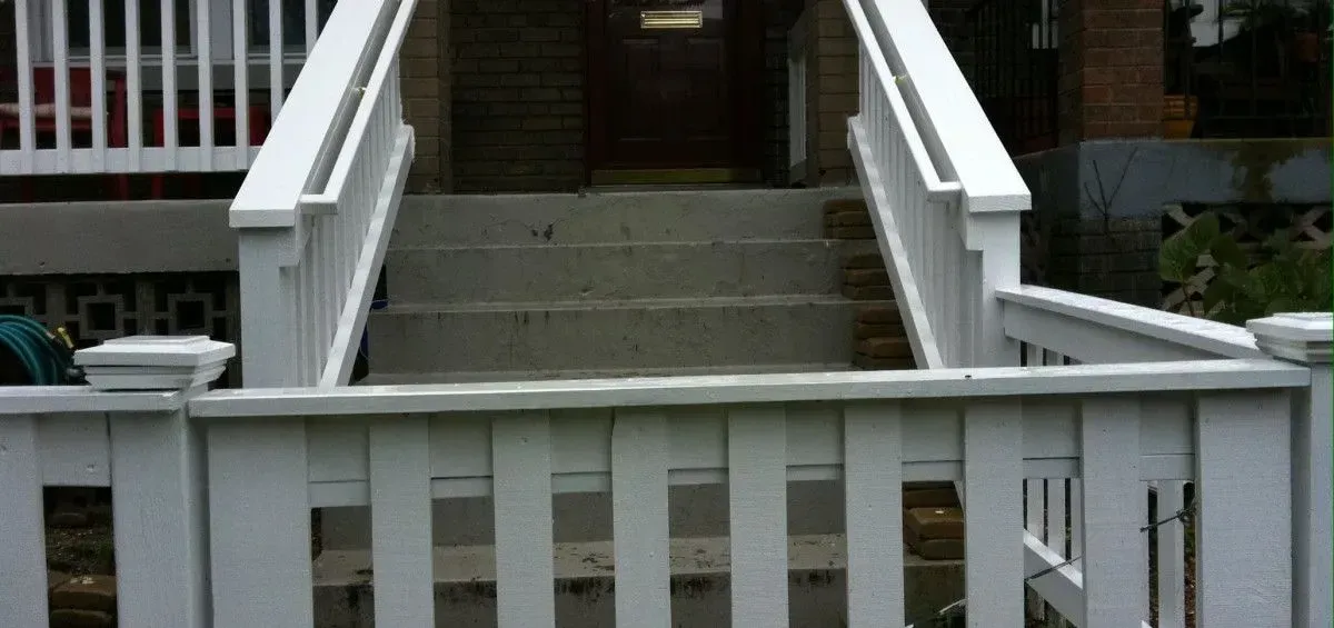 White picket fence and stairs leading to a doorway. White railing on both sides of the stairs.