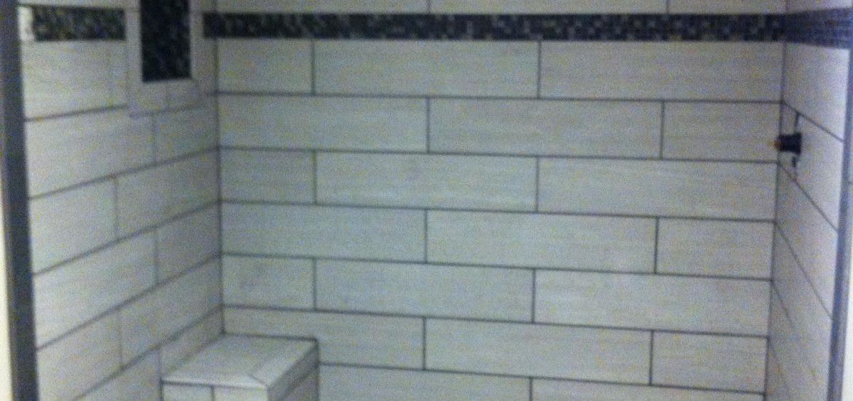 Tiled shower with a bench, dark mosaic border, and black fixtures.
