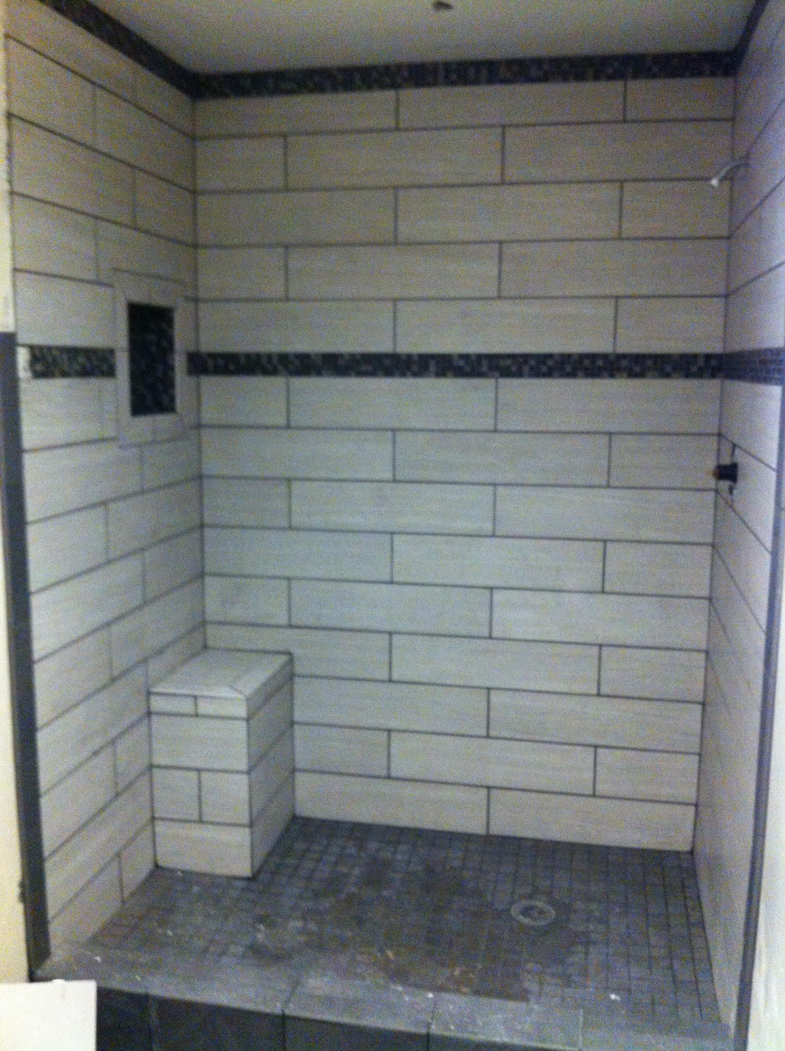 Tile-walled shower with a built-in seat and shelf. Gray and black tile.