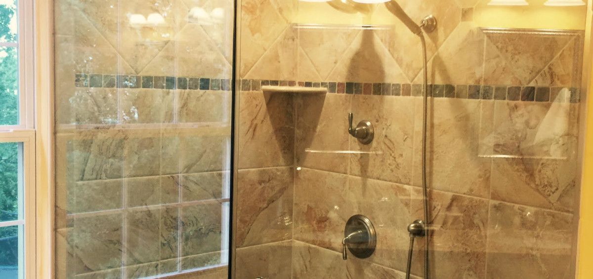 Shower stall with marble tile, glass door, and chrome fixtures.