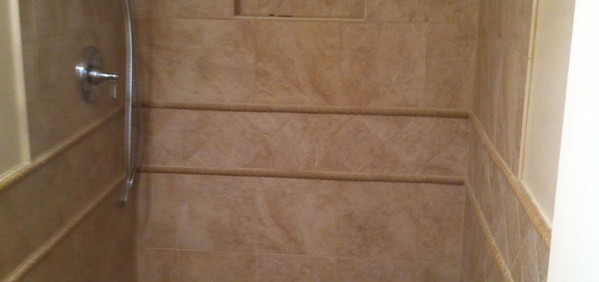 Shower stall with beige tile, chrome shower fixture.